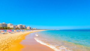 Plajă românească cu umbrele colorate și mare albastră.